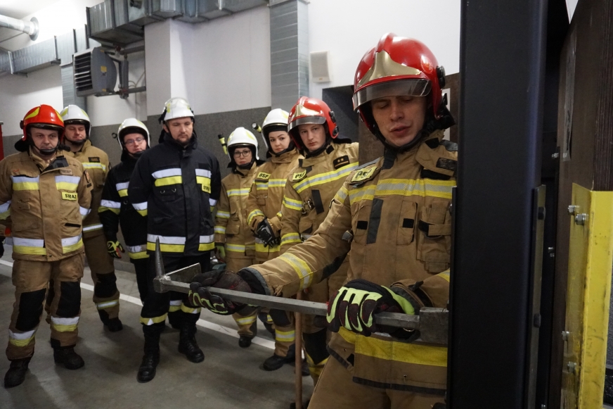 Starszy strażak Daniel Adamek z KP PSP Iława prezentuje kursantom z OSP, jak prawidłowo wyważa się drzwi Halliganem