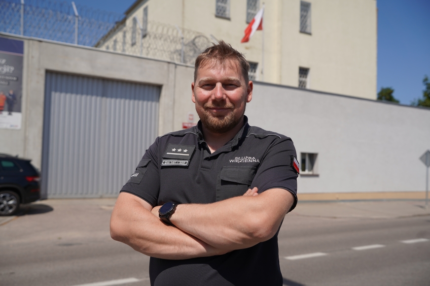 Porucznik Paweł Pierczyński, nowy rzecznik prasowy Zakładu Karnego w Iławie. W tle - iławska jednostka penitencjarna